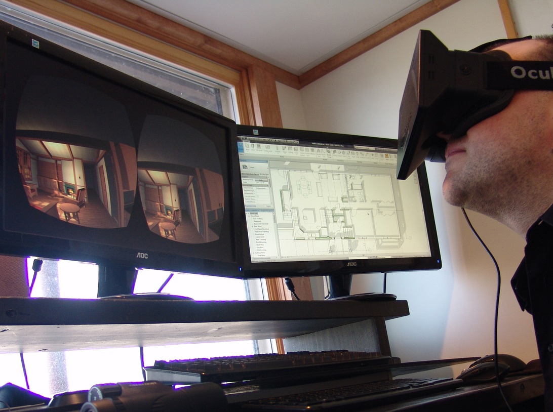 A person wearing an Oculus VR headset sitting at a computer desk with multiple monitors. The left screen shows a stereoscopic view of a virtual room interior, while the right screen displays what appears to be architectural plans or a floor layout. This clearly illustrates virtual environment technology that can be used for remote interaction and virtual relationships.