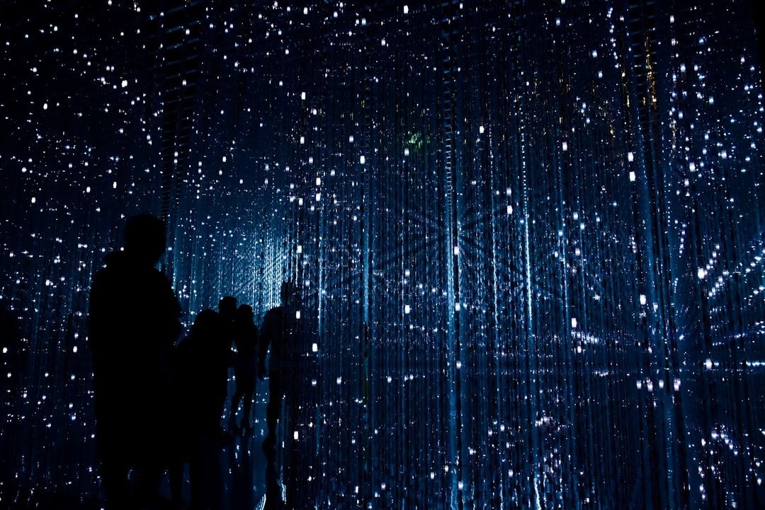 Silhouetted visitors inside a dark, blue-lit digital art installation
